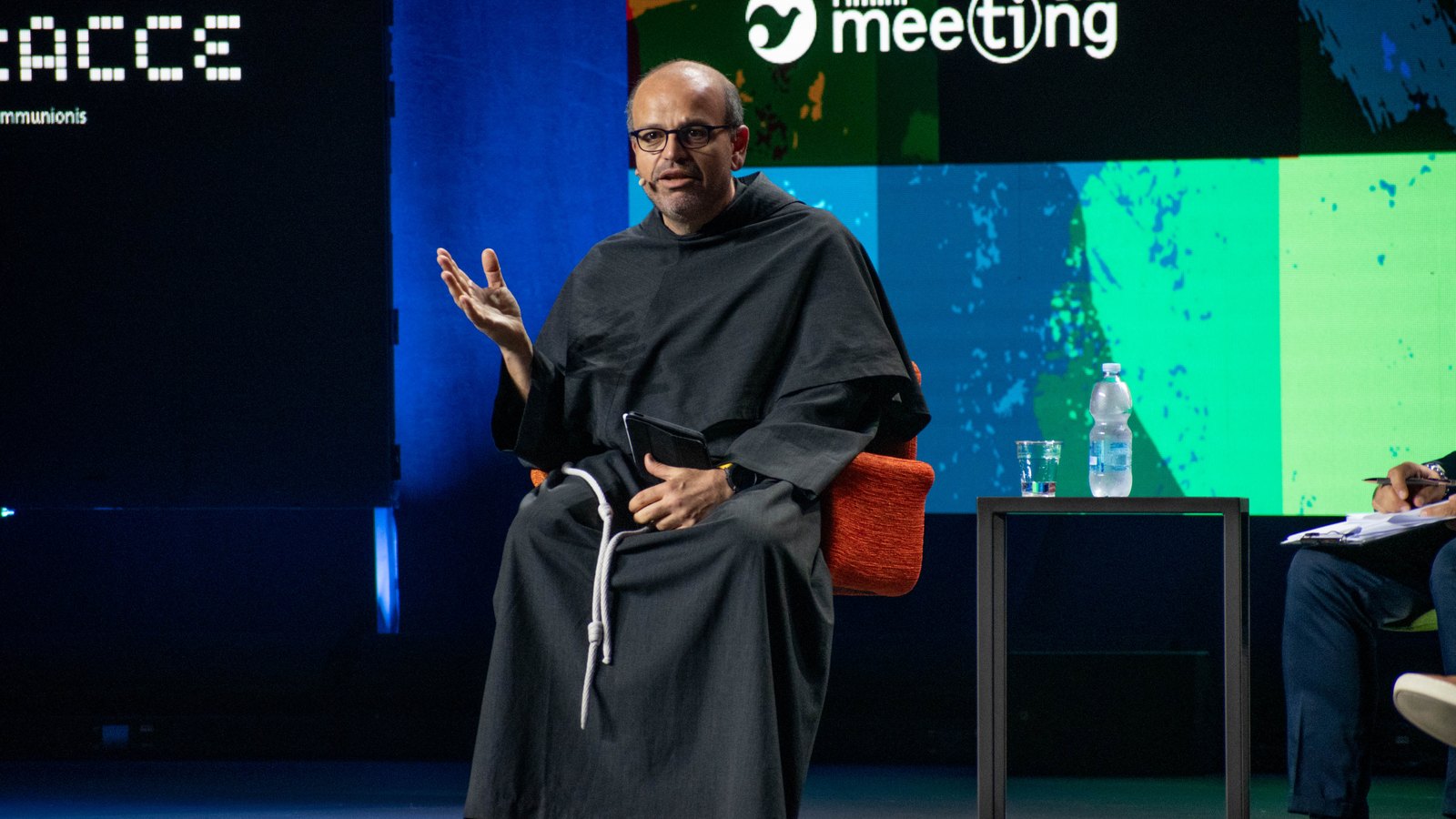 Father Paolo Benanti in a Franciscan habit speaking on stage at the Rimini Meeting in 2022